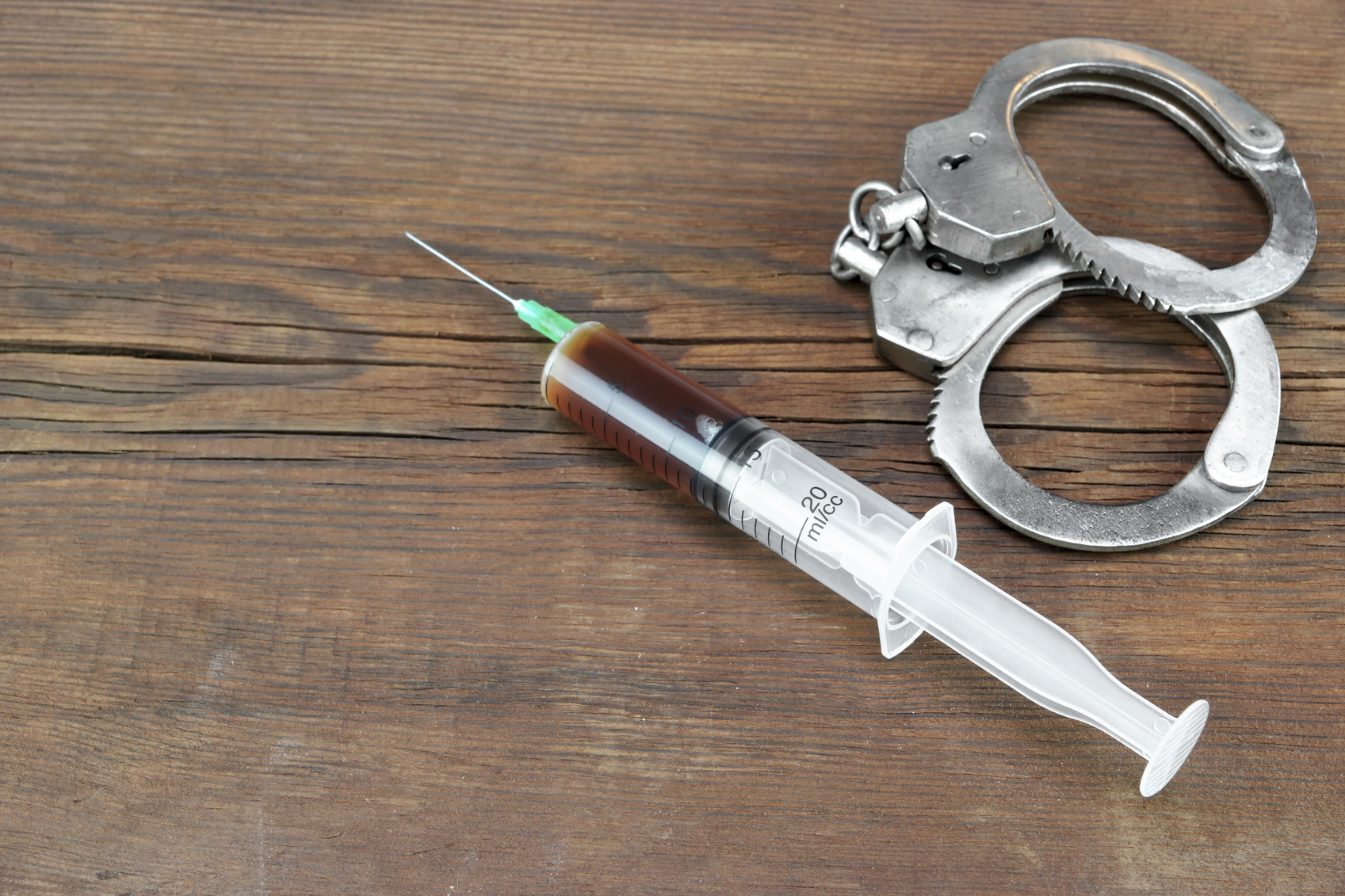 Medical Syringe And Handcuffs On The Wooden Table