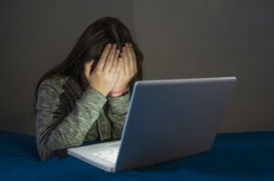 Sad and scared female teenager with computer laptop suffering cyberbullying and harassment being online feeling desperate and humiliated