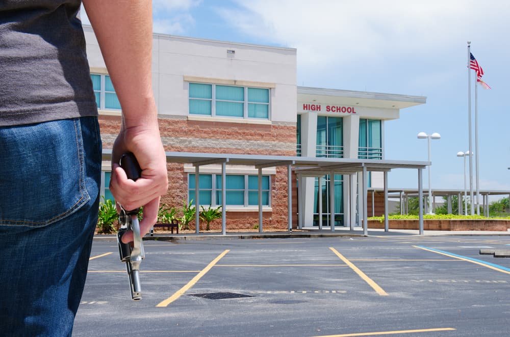 A young man with a pistol gun is standing in front of a high school preparing to commit a crime