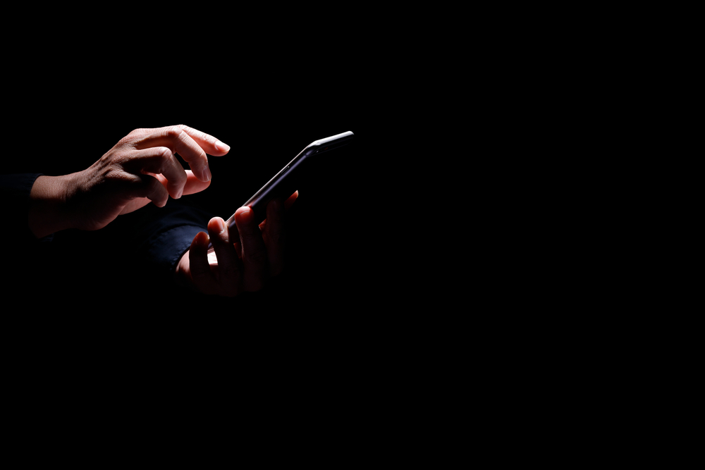 A hand holding a cellphone representing the article's topic about Posting Harmful Information on the Internet PC 653.2