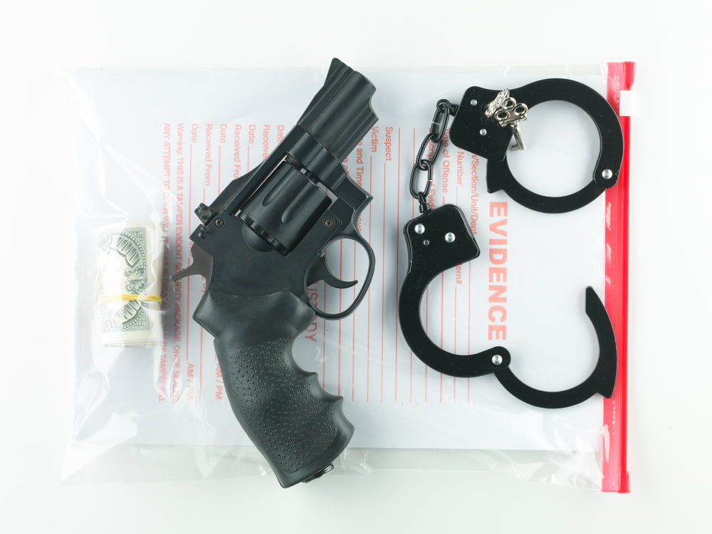 a bag marked evidence containing a roll of money, a revolver and a pair of handcuffs illustrating the article about what is a felony