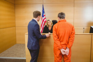 Lawyer and judge speaking next to the criminal in handcuffs in the court room representing the article about What Makes a Good Criminal Defense Lawyer