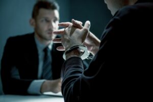 Criminal man with handcuffs being interviewed in interrogation room after committed a crime